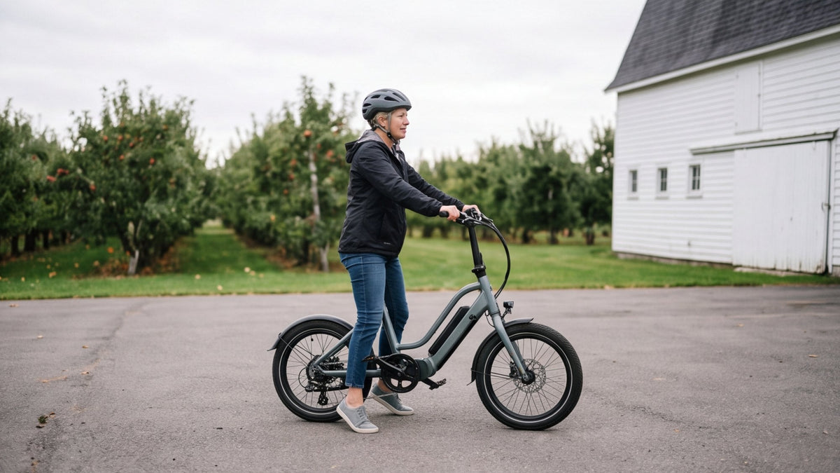 Rider in a helmet standing flat-footed over a low step-through e-bike in a farmhouse yard